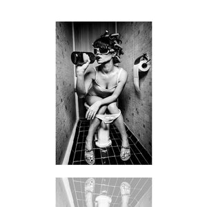 Eine Frau sitzt nach der Party auf der Toilette und trinkt aus der Flasche. Sie hat Lockenwickler in den Haaren und sie trägt eine übergroße Brille