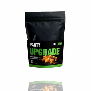 Party Upgrade, handgemachtes Gourmet Popcorn von Pottkorn steht auf einer schwarzen Tüte mit einer grünen Banderole.