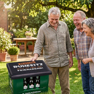 Neben einem Rentner steht ein Bierasten mit einem Bierkastensitz darauf. Drei Rentner schauen das Geschenk für den Rentner an.