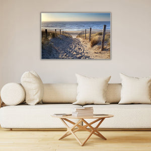 Auf einem Kunstdruck mit Rahmen ist eine Dünenlandschaft zu sehen. Im Hintergrund sieht man das Meer. Das Bild hängt an einer Wand über dem Sofa