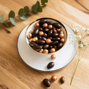 In einer Schüssel befindet sich Cashewkerne mit dunkler Schokolade, Mandeln mit heller Schokolade und Getreidekugeln in der Farbe Bronze. Knuspermix von Jalalldor.