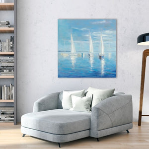 Ein hellgraues, modernes Chaiselongue-Sofa mit passenden Kissen steht in einem modern gestalteten Wohnzimmer. An einer rustikalen Betonwand über dem Sofa hängt ein großes, quadratisches Gemälde im maritimen Stil, das Segelboote auf dem Meer zeigt. Links ist ein Bücherregal mit verschiedenen Büchern zu sehen, rechts eine Stehlampe mit einem Holzstativ.
