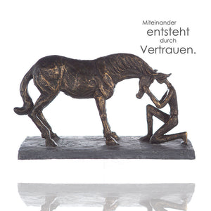 Die Dekofigur zeigt ein Pferd und einen Reiter der vor dem Pferd kniet. Miteinander entsteht durch Vertrauen.