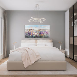 Über einem Bett hängt im hellen Schlafzimmer ein Bild von einer Landschaft der Toskana oder Provance. Eine bunte Blumenwiese ziert die hügelige Landschaft mit dem Dorf. Ein ideales Bild im Querformat für ein Schlafzimmer.