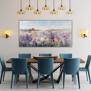 In einem Esszimmer mit petrolfarbenen Stühlen und einem Holztisch hängt eine Gemälde der Toskana oder Provance an der Wand. Auf dem Gemälde im Querformat sieht man eine bunte Blumenwiese und ein Dorf in der hügeligen Landschaft.