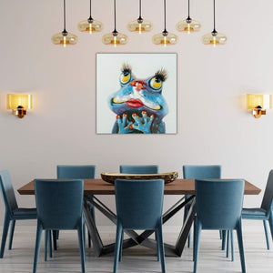 In einem Esszimmer hängt ein Bild von einer verliebten Froschdame. Der frosch ist blau, hat große Wimpern und einen Kussmund.