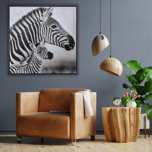Eine graue Wand vor dem ein brauner Sessel steht. An der Wand hängt ein schwarz weiß Gemälde mit einem Zebra und einem Zebrafohlen. das afrikanische Gemälde strahlt Ruhe aus.
