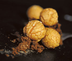 Goldgelber Mushroom Popcorn liegt neben Zimt auf einem schwarzen Tisch. Das Popcorn ist von der Marke Pottkorn.