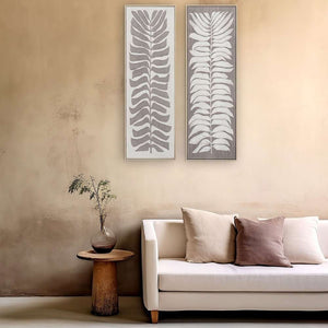 Zwei schmale gerahmte Bilder die genau aufeinander abgestimmt sind hängen an einer sandfarbenen Wand. Auf den Gemälden sind Blätter zu sehen.