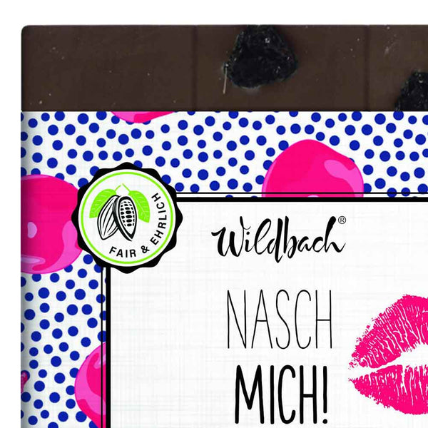 Die Wildbach Vollmilchschokolade mit Sauerkirschen hat eine wunderschöne Verpackung. Auf der Verpackung steht Nasch Mich und daneben ist ein pinkfarbener Kussmund abgebildet. Verführerisch.